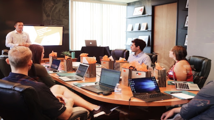 A manager discussing intelligent search with a team at a conference table with laptops.